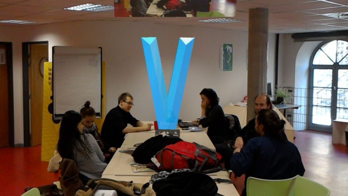 Un V majuscule flotte sur une table au milieu d'un groupe de travail