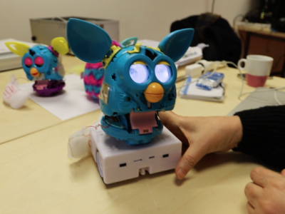 Un Furby aux yeux allumés se tient sur un robot Thymio