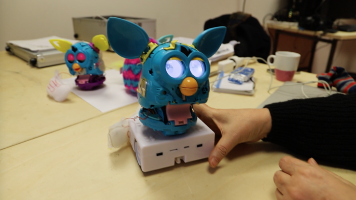 Un Furby aux yeux allumés se tient sur un robot Thymio